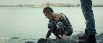 Movie still from “Suburra” (2015), directed by Stefano Sollima – A woman kneeling on a rock near the water; Medium shot, High angle