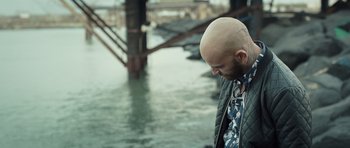 Movie still from “Suburra” (2015), directed by Stefano Sollima – A man with a bald head standing next to a body of water; Close Up shot, High angle
