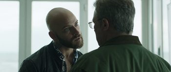 Movie still from “Suburra” (2015), directed by Stefano Sollima – A man with a bald head is looking at a man with glasses; Close Up shot, Over the shoulder angle