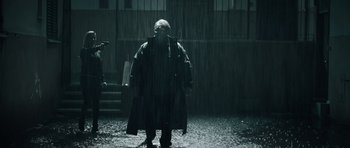 Movie still from “Suburra” (2015), directed by Stefano Sollima – A man standing in the rain wearing a raincoat; Wide shot, Low angle