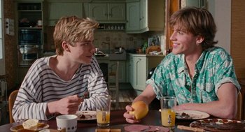 Movie still from “Summer of 85” (2020), directed by François Ozon – Two young men sitting at a table with food and drinks; Medium shot, Over the shoulder angle