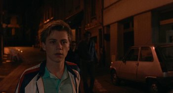 Movie still from “Summer of 85” (2020), directed by François Ozon – A young man standing on the side of the street at night; Close Up shot, Over the shoulder angle
