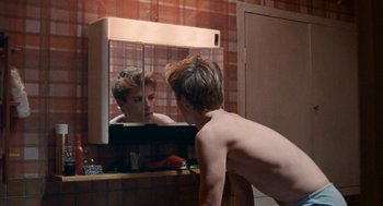 Movie still from “Summer of 85” (2020), directed by François Ozon – A man looking at himself in the mirror in a bathroom; Medium shot, Over the shoulder angle
