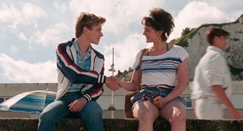 Movie still from “Summer of 85” (2020), directed by François Ozon – A man and a woman sitting on a bench shaking hands; Medium shot, Over the shoulder angle