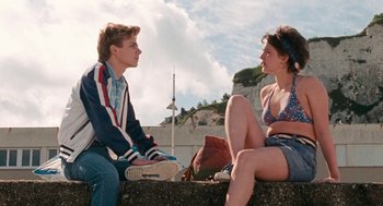 Movie still from “Summer of 85” (2020), directed by François Ozon – Two young people sitting on a ledge talking; Medium shot, Low angle