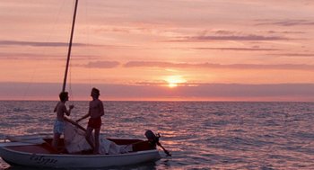 Movie still from “Summer of 85” (2020), directed by François Ozon – A person standing on a boat in the ocean at sunset; Extreme Wide shot, Low angle
