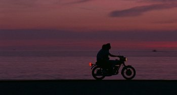 Movie still from “Summer of 85” (2020), directed by François Ozon – A person riding a motorcycle on a beach at night; Extreme Wide shot, Low angle
