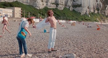 Movie still from “Summer of 85” (2020), directed by François Ozon – A man standing on a beach holding a towel; Wide shot, Low angle