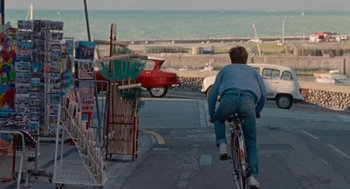 Movie still from “Summer of 85” (2020), directed by François Ozon – A man riding a bike down a street; Wide shot, High angle
