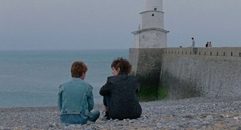 Movie still from “Summer of 85” (2020), directed by François Ozon – Two people sitting on the beach looking at a light house; Wide shot, Over the shoulder angle