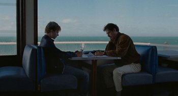 Movie still from “Summer of 85” (2020), directed by François Ozon – Two people sitting at a table with a glass of wine; Medium shot, Over the shoulder angle