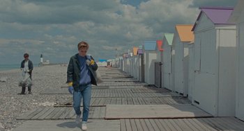 Movie still from “Summer of 85” (2020), directed by François Ozon – A man walking down a sidewalk near a row of beach huts; Wide shot, High angle