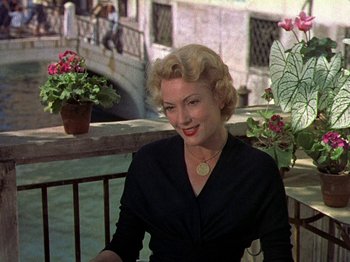 Movie still from “Summertime” (1955), directed by David Lean – A woman sitting on a bench in front of a bridge; Medium shot, High angle