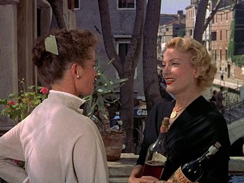 Movie still from “Summertime” (1955), directed by David Lean – Two women standing next to each other holding wine bottles; Medium shot, Over the shoulder angle