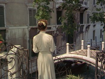 Movie still from “Summertime” (1955), directed by David Lean – A woman in a white dress standing in front of a bridge; Wide shot, High angle