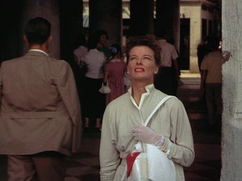 Movie still from “Summertime” (1955), directed by David Lean – An older woman is standing in front of a group of people; Medium shot, Low angle