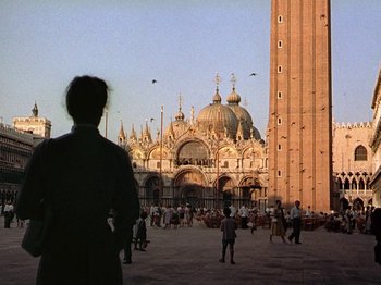 Movie still from “Summertime” (1955), directed by David Lean – A man standing in front of a building with people walking around it; Extreme Wide shot, Low angle