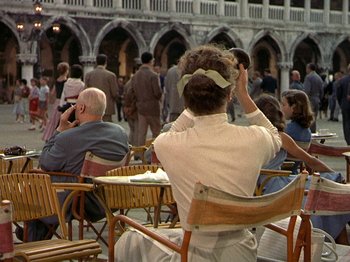 Movie still from “Summertime” (1955), directed by David Lean – A group of people sitting in chairs in a courtyard; Wide shot, Over the shoulder angle