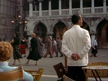 Movie still from “Summertime” (1955), directed by David Lean – A man in a white jacket standing in front of a crowd of onlookers; Wide shot, Over the shoulder angle