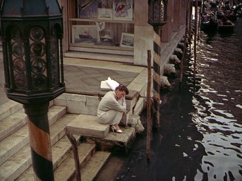 Movie still from “Summertime” (1955), directed by David Lean – A man sitting on steps in front of a building; Wide shot, High angle