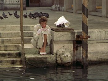 Movie still from “Summertime” (1955), directed by David Lean – A woman sitting on steps near a body of water; Wide shot, High angle