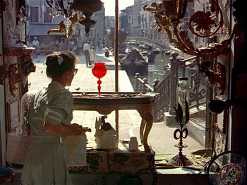 Movie still from “Summertime” (1955), directed by David Lean – A woman standing at a table looking out of a shop window; Wide shot, High angle