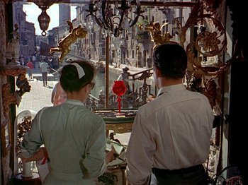 Movie still from “Summertime” (1955), directed by David Lean – A man and a woman are looking at statues in a shop window; Wide shot, High angle