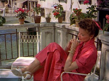 Movie still from “Summertime” (1955), directed by David Lean – A woman sitting on a chair on a balcony; Wide shot, High angle