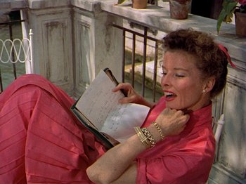 Movie still from “Summertime” (1955), directed by David Lean – A woman in a pink dress holding an open book; Medium shot, High angle