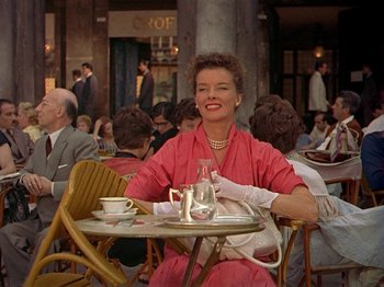Movie still from “Summertime” (1955), directed by David Lean – A woman sitting at an outdoor table with a cup of coffee; Medium shot, Low angle