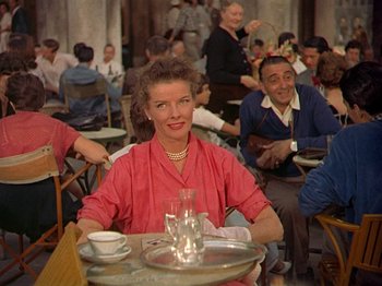 Movie still from “Summertime” (1955), directed by David Lean – A woman sitting at a table with a tray of food; Medium shot, Over the shoulder angle