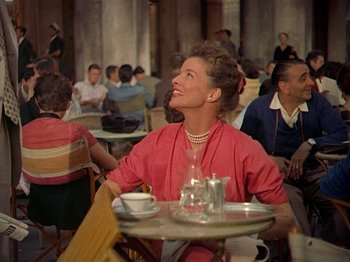 Movie still from “Summertime” (1955), directed by David Lean – A woman sitting at a table with a glass of wine; Medium shot, Low angle