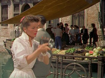 Movie still from “Summertime” (1955), directed by David Lean – A woman in a white dress is holding a plate; Medium shot, Low angle