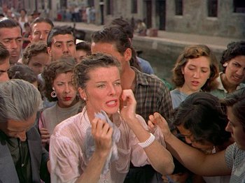 Movie still from “Summertime” (1955), directed by David Lean – A group of people standing next to each other on the street; Medium shot, Over the shoulder angle