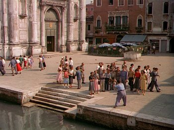 Movie still from “Summertime” (1955), directed by David Lean – A group of people standing around a body of water; Extreme Wide shot, High angle