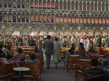 Movie still from “Summertime” (1955), directed by David Lean – A group of people standing in a room with tables and chairs; Extreme Wide shot, High angle
