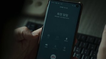 Movie still from “Hellbound” (2021), created by Yeon Sang-ho – A person holding a smart phone in front of a computer keyboard; Extreme Close Up shot, High angle