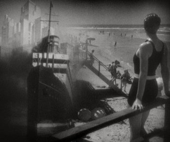 Movie still from “Sunrise” (1927), directed by F.W. Murnau – A woman in a bathing suit standing on the beach; Wide shot, High angle