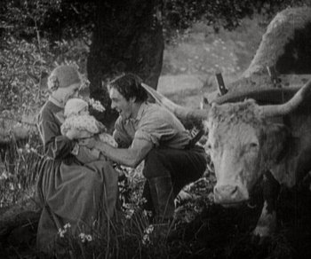 Movie still from “Sunrise” (1927), directed by F.W. Murnau – An old photo of a man holding a baby in a field; Wide shot, High angle