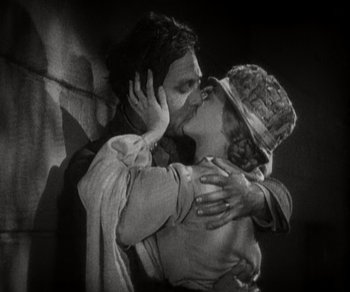 Movie still from “Sunrise” (1927), directed by F.W. Murnau – A man and a woman kissing in front of a brick wall; Medium shot, Low angle
