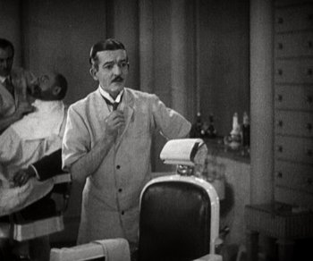 Movie still from “Sunrise” (1927), directed by F.W. Murnau – An old photo of a man standing in front of a chair; Medium shot, High angle