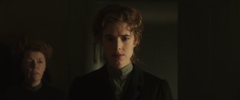 A young woman with long brown hair wearing a black suit