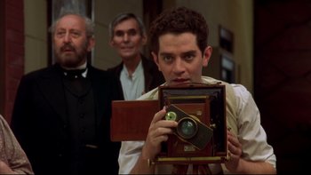 Movie still from “Sunshine” (1999), directed by István Szabó – A man holding an antique camera in front of two other men; Close Up shot, Low angle
