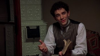 Movie still from “Sunshine” (1999), directed by István Szabó – A man holding a book in his hand while sitting in front of an oven; Medium shot, High angle