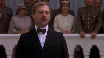 Movie still from “Sunshine” (1999), directed by István Szabó – A man wearing a suit and bow tie in front of a group of people; Close Up shot, Low angle