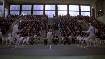 Movie still from “Sunshine” (1999), directed by István Szabó – A man standing in front of a group of people in a stadium; Extreme Wide shot, High angle