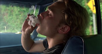 Movie still from “Super Troopers” (2001), directed by Jay Chandrasekhar – A man sitting in the back seat of a car while smoking a cigarette; Close Up shot, Low angle
