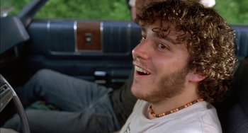 Movie still from “Super Troopers” (2001), directed by Jay Chandrasekhar – A man with a beard and a necklace is sitting in the back of a car; Close Up shot, Low angle