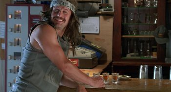 Movie still from “Super Troopers” (2001), directed by Jay Chandrasekhar – A man with long brown hair is holding a shot glass; Medium shot, Over the shoulder angle