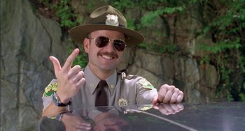 Movie still from “Super Troopers” (2001), directed by Jay Chandrasekhar – A man in a hat sitting in the back of a police car; Medium shot, Low angle